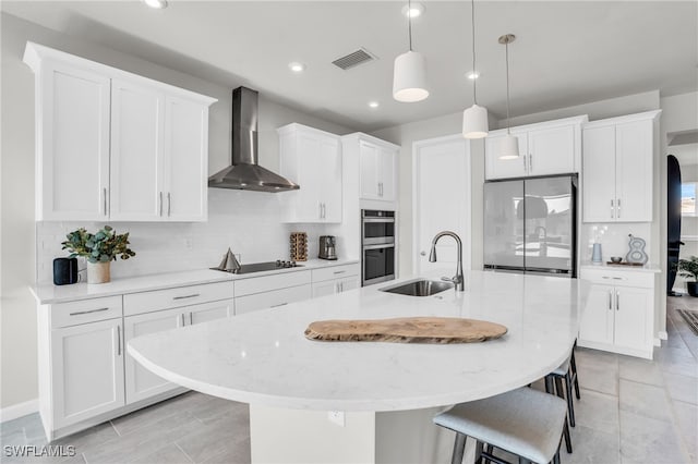 kitchen featuring sink, stainless steel appliances, a kitchen island with sink, and wall chimney range hood