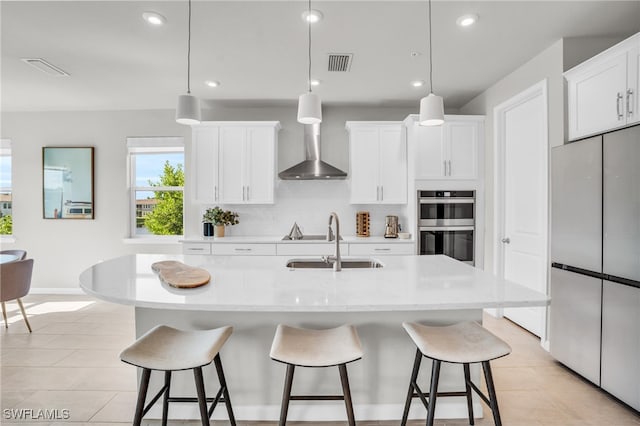 kitchen featuring a center island with sink, white cabinets, stainless steel appliances, and hanging light fixtures