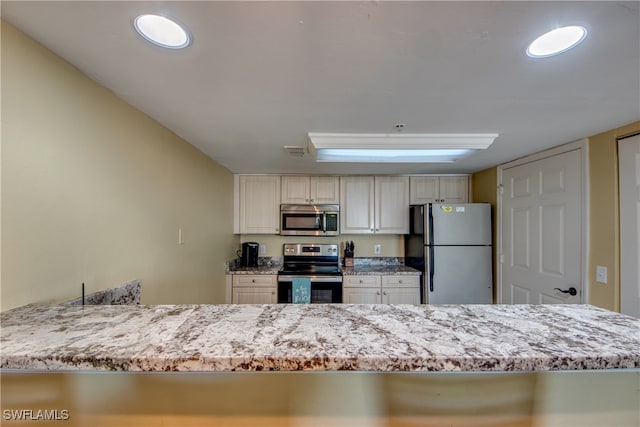 kitchen with kitchen peninsula, light stone countertops, white cabinetry, and stainless steel appliances