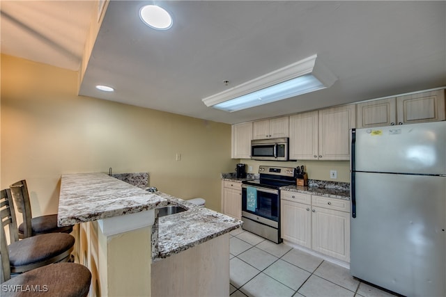 kitchen with sink, a breakfast bar area, light stone countertops, light tile patterned flooring, and stainless steel appliances