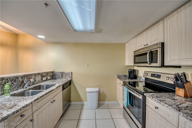 kitchen with light tile patterned flooring, appliances with stainless steel finishes, light stone counters, and sink