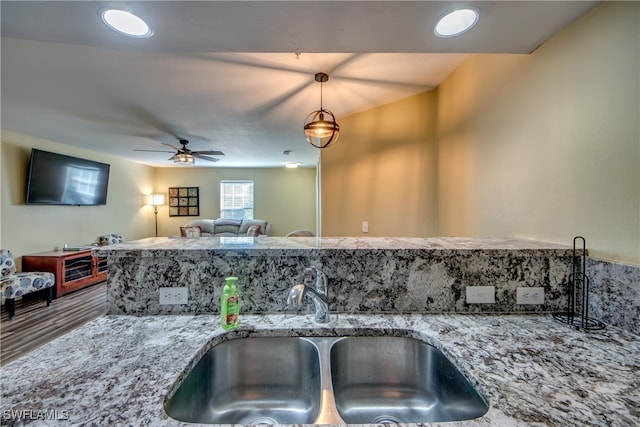 kitchen featuring hanging light fixtures, light stone counters, ceiling fan, and sink