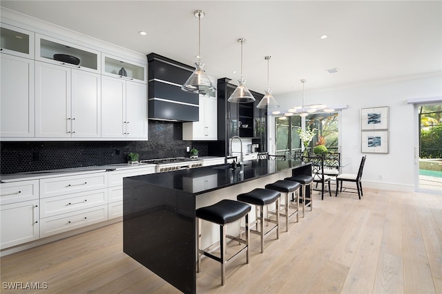 kitchen with decorative backsplash, a center island with sink, light hardwood / wood-style floors, and decorative light fixtures