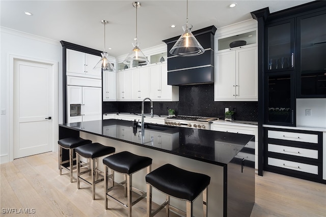 kitchen featuring pendant lighting, light hardwood / wood-style flooring, decorative backsplash, ornamental molding, and an island with sink