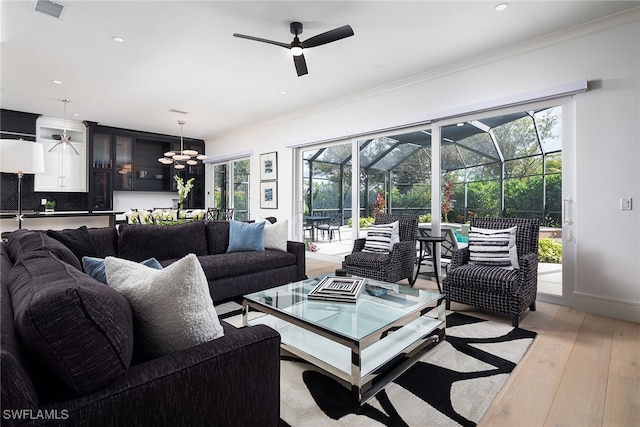 living room with crown molding, light hardwood / wood-style flooring, a healthy amount of sunlight, and ceiling fan with notable chandelier