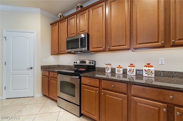 kitchen featuring light tile patterned floors, ornamental molding, appliances with stainless steel finishes, and dark stone counters