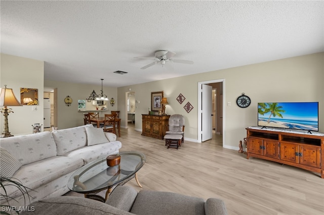 living room with ceiling fan with notable chandelier, light wood-type flooring, and a textured ceiling