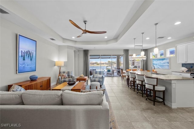 tiled living room featuring a raised ceiling, ceiling fan, and sink