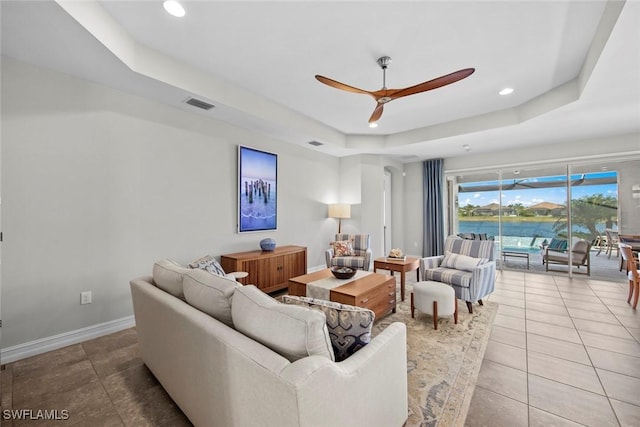 tiled living room with ceiling fan and a raised ceiling