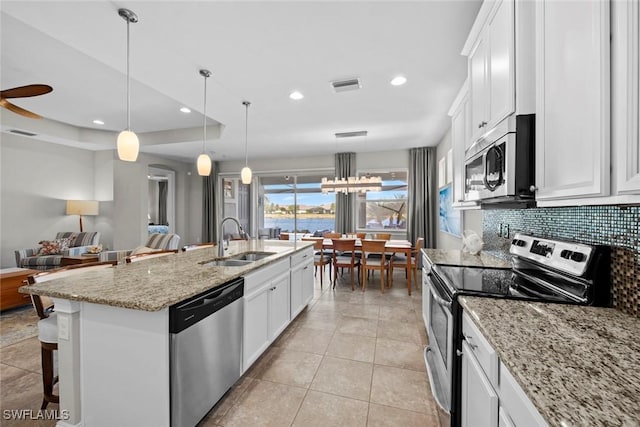 kitchen with appliances with stainless steel finishes, a kitchen island with sink, sink, white cabinetry, and hanging light fixtures