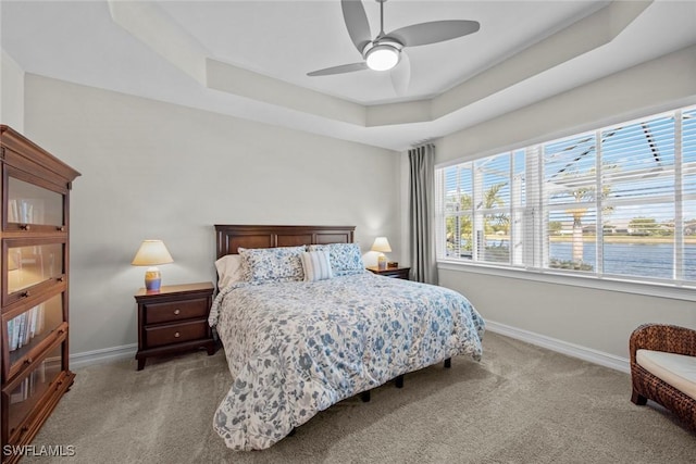 carpeted bedroom featuring ceiling fan, a raised ceiling, and multiple windows