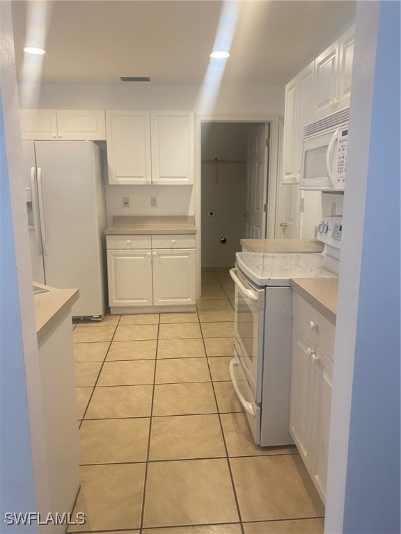 kitchen with white appliances, white cabinetry, and light tile patterned flooring