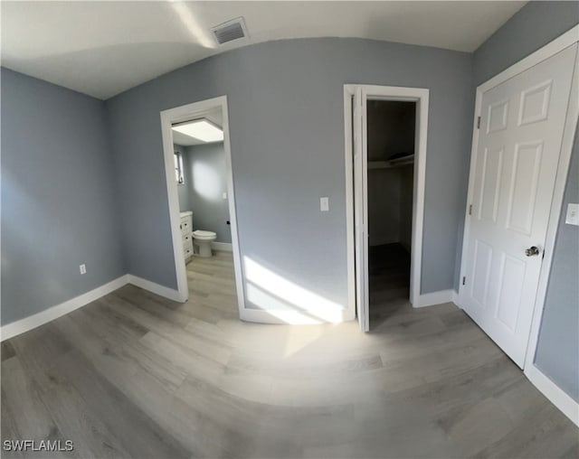 unfurnished bedroom featuring a walk in closet, light hardwood / wood-style flooring, a closet, and connected bathroom