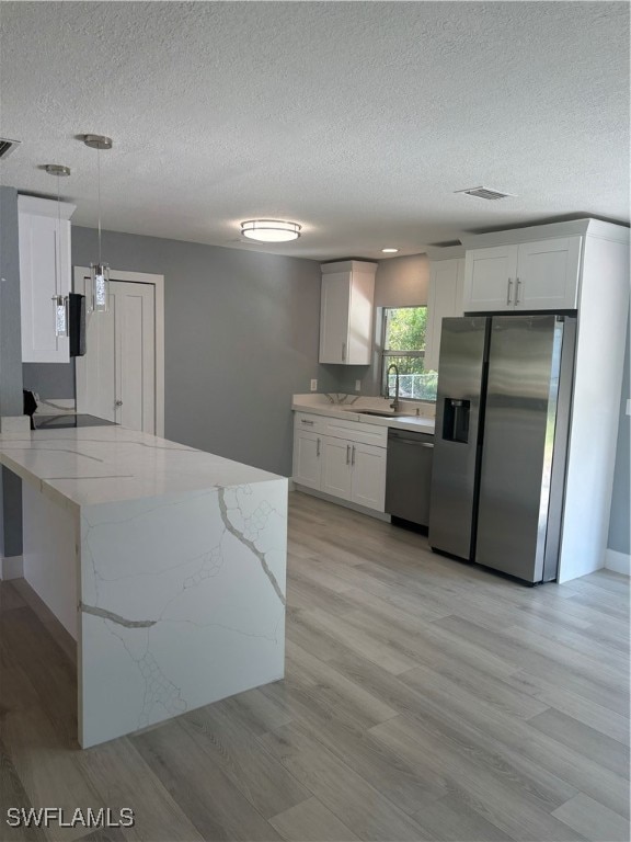 kitchen with white cabinetry, hanging light fixtures, light hardwood / wood-style flooring, a textured ceiling, and appliances with stainless steel finishes