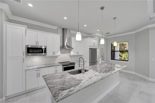 kitchen with wall chimney range hood, sink, an island with sink, appliances with stainless steel finishes, and decorative light fixtures