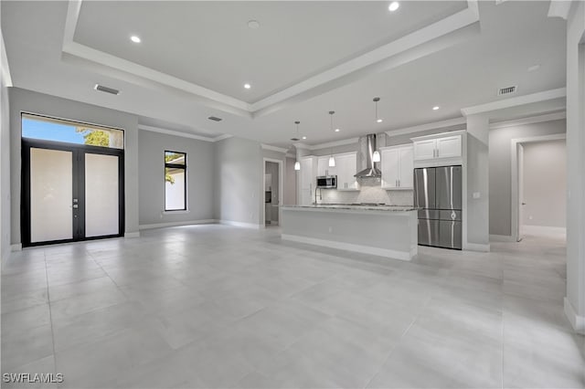 unfurnished living room featuring a raised ceiling, sink, french doors, and ornamental molding