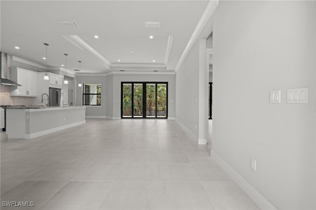 unfurnished living room with ornamental molding, sink, light tile patterned floors, and a tray ceiling