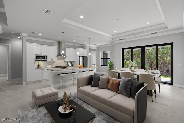 living room with a raised ceiling, crown molding, sink, and light tile patterned floors