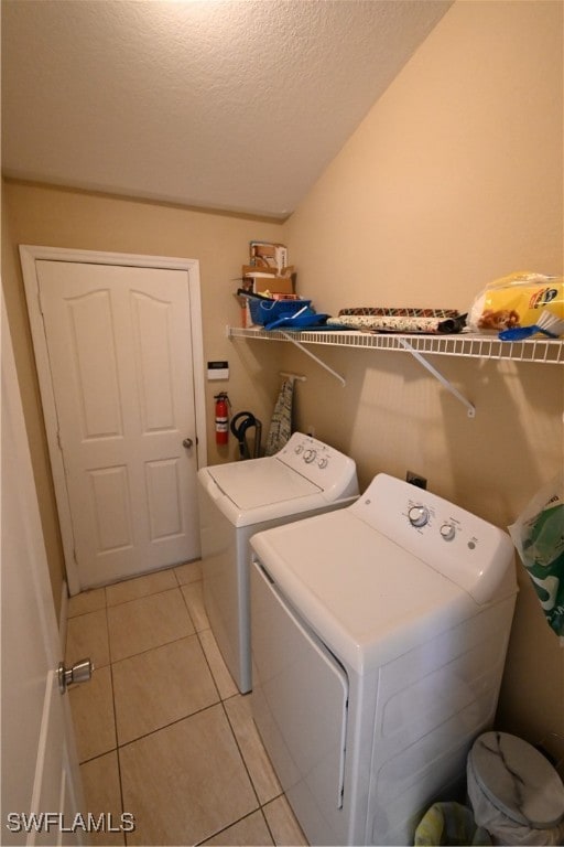 clothes washing area with washer and clothes dryer, light tile patterned floors, and a textured ceiling