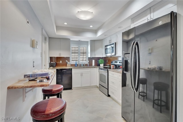 kitchen featuring decorative backsplash, appliances with stainless steel finishes, a raised ceiling, sink, and white cabinetry