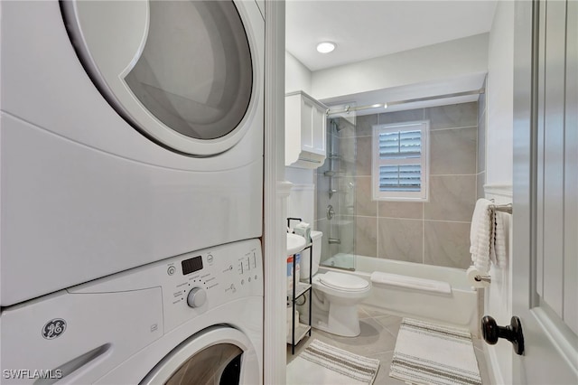 bathroom featuring combined bath / shower with glass door, tile patterned flooring, stacked washing maching and dryer, and toilet