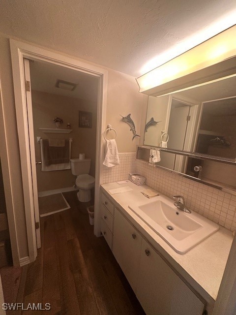 bathroom featuring vanity, hardwood / wood-style flooring, decorative backsplash, toilet, and a textured ceiling