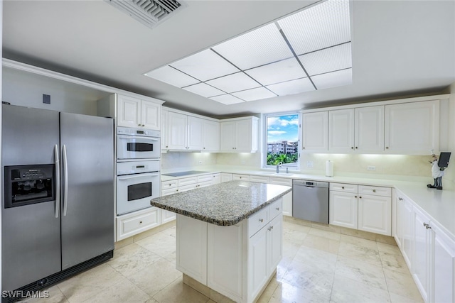 kitchen featuring white cabinets, sink, light stone countertops, appliances with stainless steel finishes, and a kitchen island