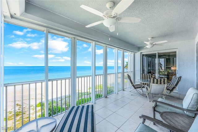 sunroom / solarium featuring ceiling fan, a water view, and a view of the beach