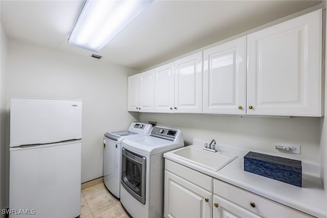 clothes washing area with washer and dryer, cabinets, light tile patterned floors, and sink