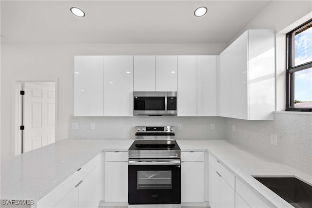 kitchen with white cabinets, light stone countertops, stainless steel appliances, and tasteful backsplash