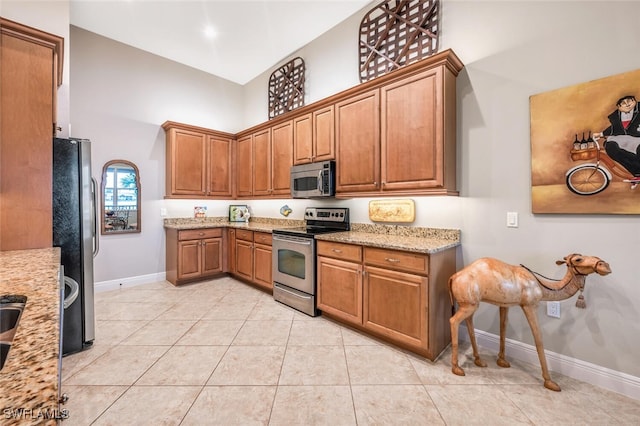 kitchen featuring light tile patterned floors, light stone countertops, a high ceiling, and appliances with stainless steel finishes