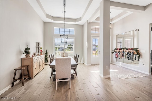 dining space featuring a high ceiling, light hardwood / wood-style flooring, a raised ceiling, and a notable chandelier