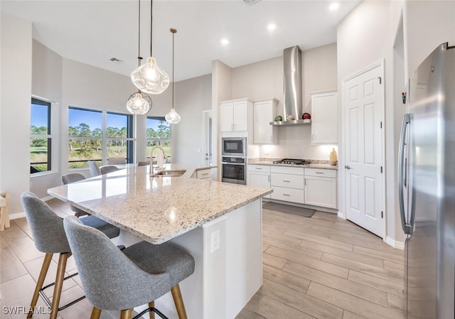 kitchen with a center island with sink, wall chimney exhaust hood, white cabinetry, and appliances with stainless steel finishes