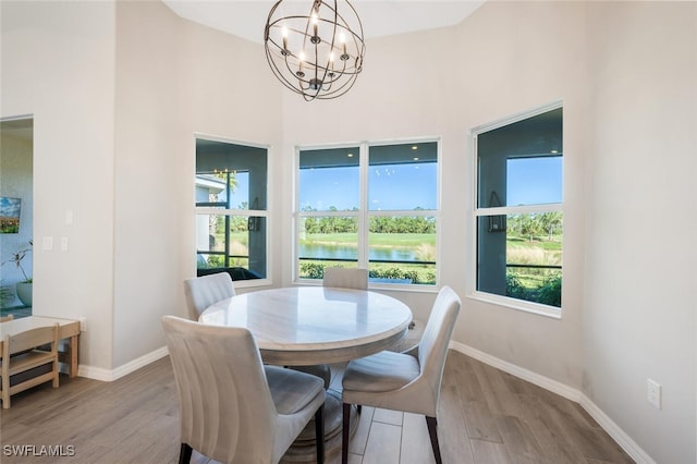 dining room featuring a high ceiling, an inviting chandelier, a water view, and light hardwood / wood-style flooring