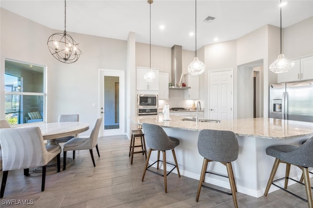 kitchen with appliances with stainless steel finishes, sink, white cabinets, hanging light fixtures, and an island with sink