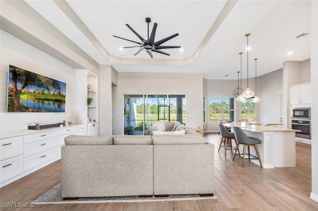 living room featuring a raised ceiling, ceiling fan, light hardwood / wood-style flooring, and sink