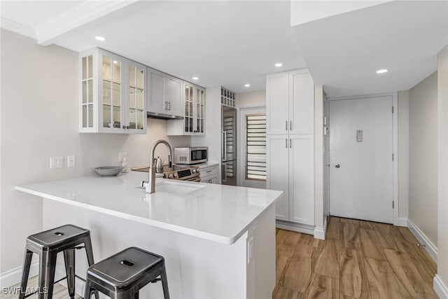 kitchen with kitchen peninsula, a kitchen breakfast bar, light wood-type flooring, and sink