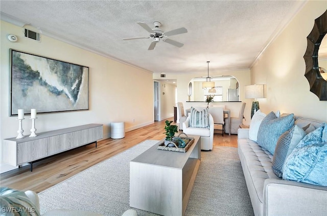 living room featuring ceiling fan, crown molding, a textured ceiling, and light wood-type flooring