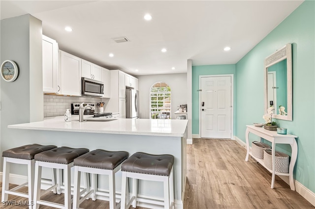 kitchen with white cabinetry, kitchen peninsula, light hardwood / wood-style floors, decorative backsplash, and appliances with stainless steel finishes