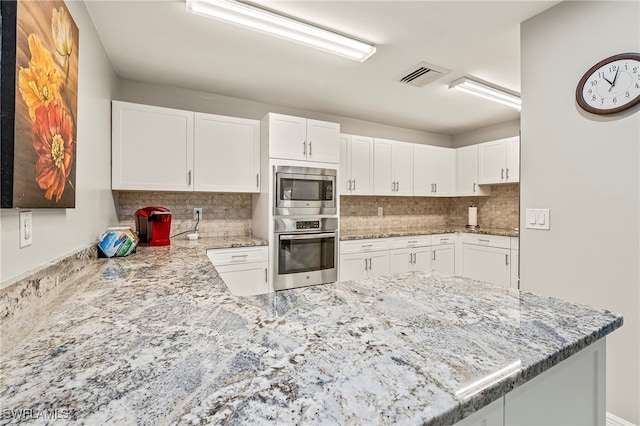 kitchen featuring kitchen peninsula, white cabinetry, decorative backsplash, and appliances with stainless steel finishes