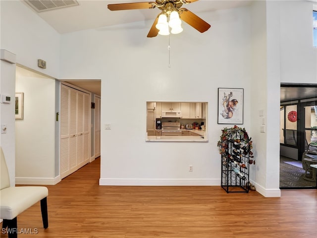 living room with ceiling fan, light hardwood / wood-style floors, and high vaulted ceiling