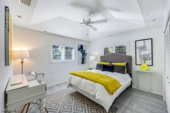 bedroom with hardwood / wood-style floors, a tray ceiling, multiple windows, and ceiling fan