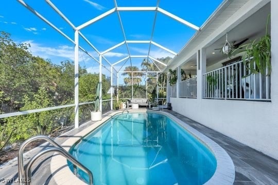 view of pool featuring glass enclosure, ceiling fan, and a patio