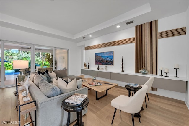 living room featuring a tray ceiling, visible vents, light wood finished floors, and recessed lighting