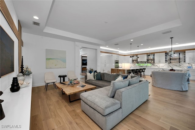 living room featuring light wood-type flooring, a raised ceiling, visible vents, and recessed lighting