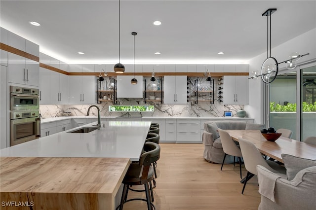 kitchen featuring pendant lighting, light countertops, white cabinetry, a sink, and an island with sink