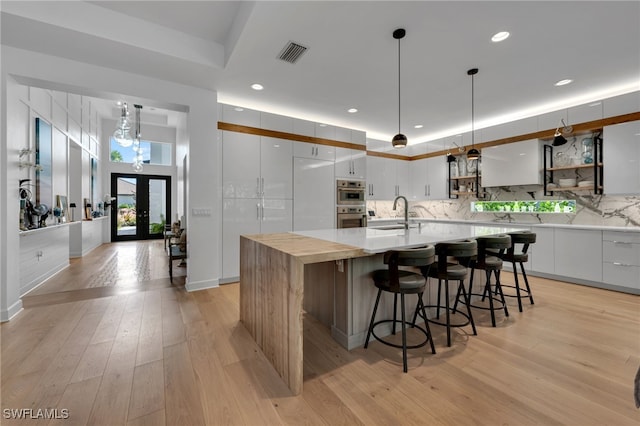 kitchen with visible vents, white cabinetry, french doors, a center island with sink, and pendant lighting