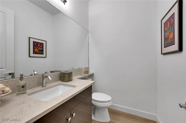 half bathroom featuring toilet, vanity, baseboards, and wood finished floors