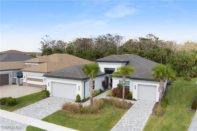 view of front of property with a garage, a tile roof, decorative driveway, a front yard, and stucco siding