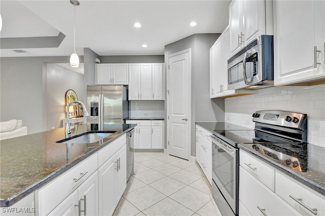 kitchen with appliances with stainless steel finishes, sink, dark stone countertops, white cabinets, and hanging light fixtures